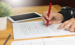 hand holding red pen on manuscript pages